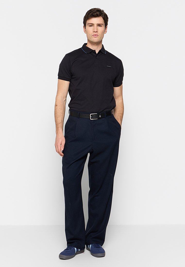 Camisa polo negra con acentos azules, combinada con pantalones azul marino. El conjunto presenta un corte clásico y zapatillas casuales.