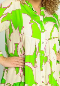 Groene en crème jurk met een bloemenprint in het roze, voorzien van een knoopsluiting aan de voorkant, kraag en geplooide zoom, gemaakt van een lichtgewicht stof.