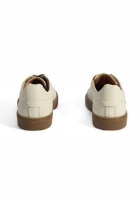 Helle beige Lederschuhe mit einer abgerundeten Zehenpartie und einer tanfarbenen Gummisohle. Sie verfügen über ein strukturiertes Obermaterial und eine dekorative Hinterlasche.