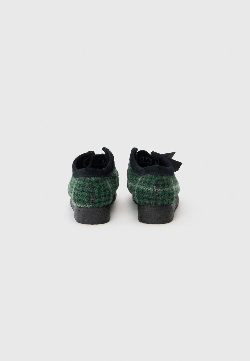 Green and black patterned footwear with a textured surface, rounded shape, and a small heel. Features a bow detail at the back.