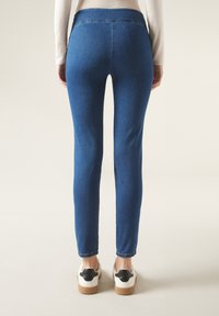 Siniset denimin skinny-farkut, joissa on korkea vyötärö, sileä pintakuvio ja vähäiset ompeleet. Asu viimeistelty valkoisilla kengillä ja mustilla yksityiskohdilla.