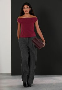 Burgundijas krāsas off-shoulder tops, kas saskan ar pelēkajiem augstās jostasvietas biksēm. Modelis tur tumši burgundijas krāsas klč. Gluda auduma struktūrēta piegrieze.