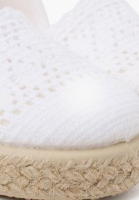 Weiße gewebte Stoffschlupfschuhe mit einer strukturierten Oberfläche, Jute-Seilsohle und sichtbaren Naturfasern entlang des Randes.