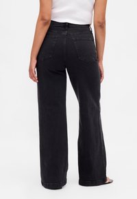 Crne široke hlače od trapera s visokim strukom, glatke teksture, pet petlji za remen i dva stražnja džepa.