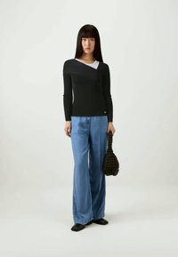 Μαύρη μπλούζα με μακριά μανίκια και ασύμμετρο λαιμόκοψη, συνδυασμένη με ανοιχτό μπλε παντελόνι με φαρδιές πόδες και μία υφασμάτινη μαύρη τσάντα. Λείος υφασμάτινος φινίρισμα.