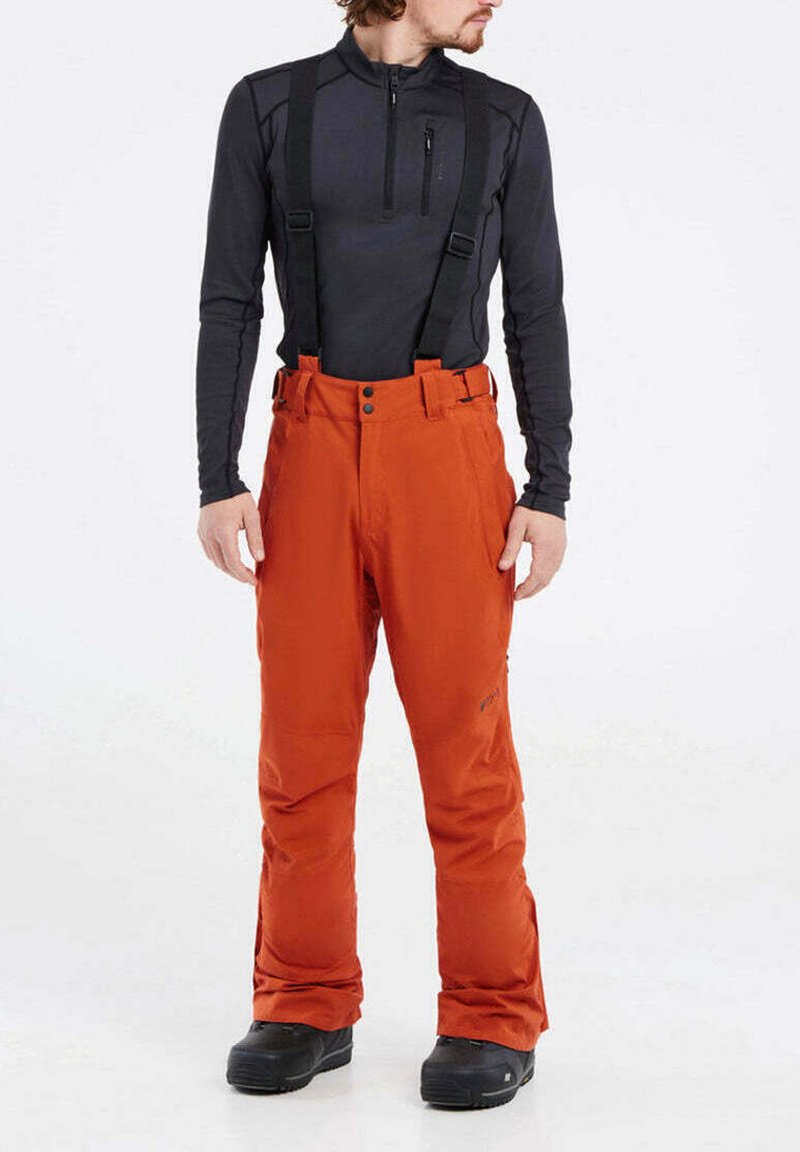 Oranga skidbyxor med justerbara hängslen, utrustade med knappar och fickor. Kombineras med en svart långärmad topp och svarta stövlar.