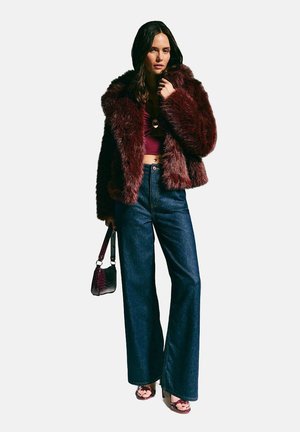 Burgundyfärgad fuskpälsjacka, kort design, tillsammans med högmidjade mörka jeans med utsvängda ben. Tillbehör inkluderar en liten handväska och klacksandaler.