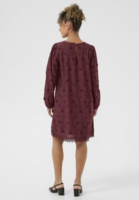 Bordeauxfarbene Kleid aus strukturiertem Stoff mit floraler Stickerei, langen Ärmeln und Spitzenbesatz am Saum, mit einem Schlüssel-ausschnitt im Rücken.