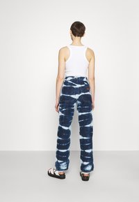 Ljusblå och mörkblå tie-dye vida jeans med hög midja, utrustade med två bakfickor och kombinerade med vita sandaler.