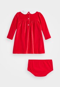 Vestido de terciopelo rojo con mangas largas, cuello blanco y cierres de botones; incluye braguitas rojas a juego. Textura suave, diseño de cintura fruncida.