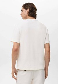 Tricou alb cu mânecă scurtă și guler rotund, dintr-un material texturat, având o croială lejeră și o margine curată. Fără logo-uri sau modele vizibile.