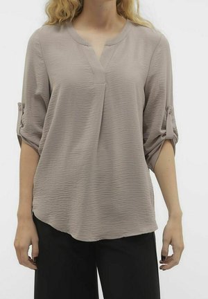 Blusa beige con texture, scollo a V, maniche a tre quarti arrotolabili e orlo curvato. Il materiale è leggero e leggermente sgualcito.
