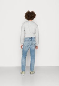 Felpa grigia con maniche lunghe, abbinata a jeans blu chiaro. Sneakers verde chiaro con suole bianche. Sfondo semplice, vista da dietro.