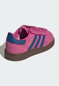 Rosa mockasneaker med blå tre ränder, rundad tå, texturerad brun gummisula, rosa skosnören och en blå hälflik.