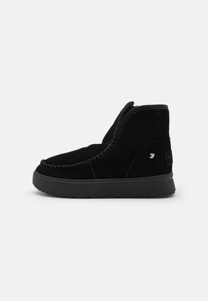 Sorte ankelboots i semsket skinn med avrundet tå, subtil søm, sidepanel og en teksturert gummisåle. Lite logodetalj bak.