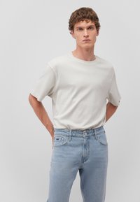 Weißes T-Shirt mit kurzen Ärmeln und rundem Ausschnitt, kombiniert mit hellblauen Jeans im Straight-Leg-Schnitt. Glattes Material, einfaches Design, ohne sichtbare Muster.