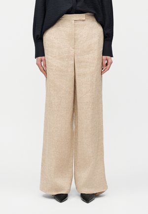 Μπεζ λινά φαρδιά παντελόνια συνδυασμένα με μαύρο μακρυμάνικο πουκάμισο και μαύρα μυτερά παπούτσια.