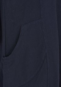 Tume sinine kangas lähivaates, kus on nähtav kõver küljetasku ja õmblused riidel.