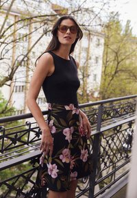 Black sleeveless top paired with a floral-patterned skirt featuring pink and green flowers on a black background. Model stands on a balcony.