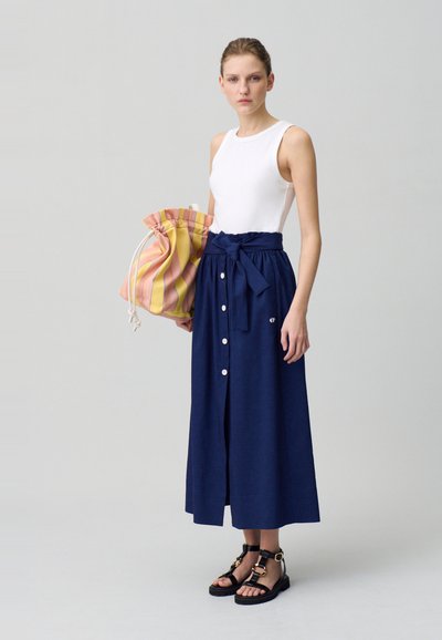 Jupe bleu marine avec des boutons et une taille à nouer, assortie à un débardeur blanc et un sac à cordon rayé en rose et jaune. Sandales noires.