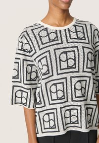 Sort og hvid top med prikker i mønster, korte ærmer og rund halsudskæring, prydet med et geometrisk print med omrids af cirkeldesigns.