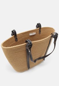 Tan vævet strandtaske med fire sorte læderhåndtag og en lille hvid mærkeetiket indeni.
