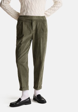 Pantalons en velours côtelé vert olive avec une coupe décontractée, dotés de poches latérales, de plis et de revers, associés à des mocassins noirs et des chaussettes blanches.