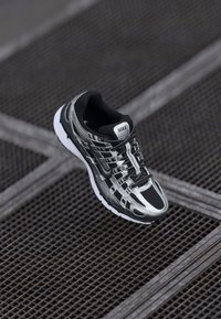 Scarpa da corsa Nike con una combinazione di colori nera e argento, tomaia in rete, suola testurizzata e sistema di allacciatura per una vestibilità sicura.