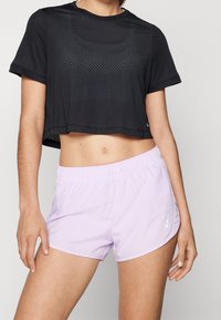 Musta lyhythihainen urheilupaita, jossa on verkkotekstuuri ja pyöreä pääntie, yhdistettynä vaaleanlilaisiin shortseihin, joissa on joustavyö ja logo.