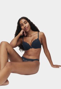 Marineblauwe kanten beha met geschulpte randen, gecombineerd met een doorschijnend kanten string. Soepel materiaal, ondersteunend ontwerp en ingewikkelde patroondetails.