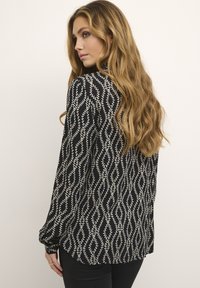 Blouse noire à manches longues avec un motif de feuilles blanches, coupe décontractée et poignets froncés. Tissu texturé avec un design fluide.