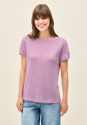 Haut lilas à manches courtes, en matière légère avec une coupe décontractée, un col rond et une texture subtile. Associé à un jean large bleu.