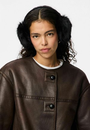 Bruine leren jack met twee zwarte knopen, witte binnenhemd zichtbaar, en zwarte nep-bont oorwarmers op het hoofd. Gladde textuur, modern ontwerp.