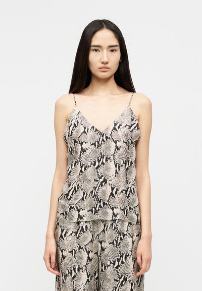 Femme aux longs cheveux foncés portant un haut sans manches à col en V et un pantalon assorti avec un motif imprimé serpent noir et blanc.