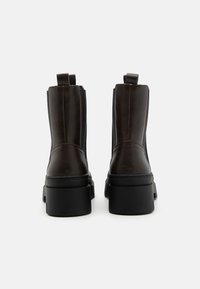 Bottines en cuir marron avec une finition texturée, semelles noires épaisses et languettes, dotées de panneaux élastiques sur les côtés pour un enfilage facile.