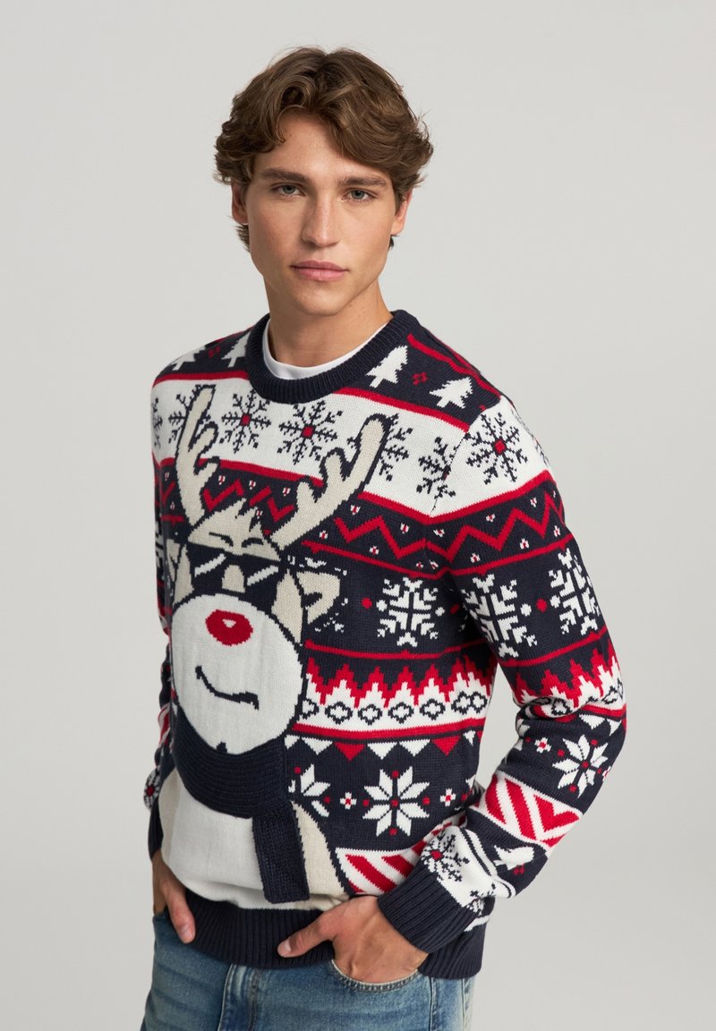 Maglione lavorato a maglia con design di renna, prevalentemente blu scuro, rosso e bianco. Decorato con fiocchi di neve, motivi geometrici e polsini a costine.