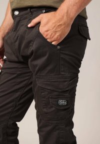 Zwarte cargobroek met een gladde textuur, voorzien van meerdere zakken en metalen accenten. Inclusief een gestikt logo-opdruk aan de zijkant.