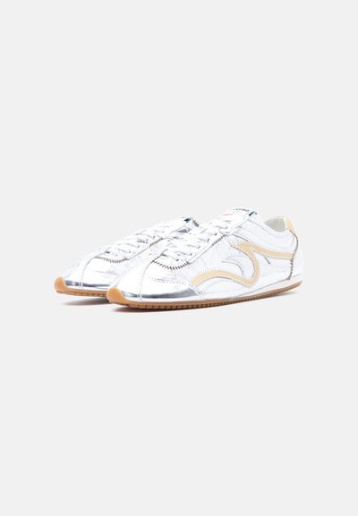 Λευκά δερμάτινα sneakers χαμηλού προφίλ με εκρού λεπτομέρειες, μπεζ λαστιχένιες σόλες και λευκά κορδόνια, εμφανιζόμενα δίπλα-δίπλα σε ανοιχτό φόντο.