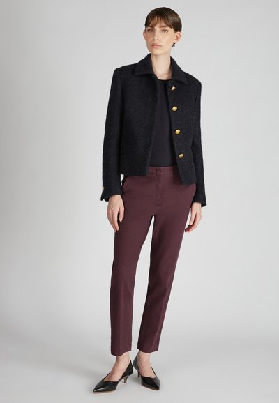 Czarna teksturowana kurtka z kołnierzykiem i złotymi guzikami, zestawiona z bordowymi spodniami slim fit i czarnymi szpilkami.
