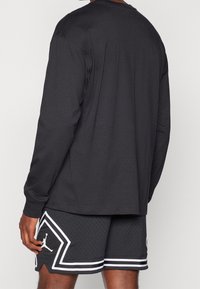 T-shirt nera a maniche lunghe con collo rotondo, abbinata a pantaloni corti neri perforati con dettagli bianchi e un logo sulla parte inferiore della gamba.