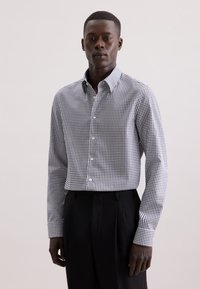 Witte overhemd met een klein zwart geruit patroon; heeft een klassieke kraag en knoopsluiting, gecombineerd met zwarte broek.