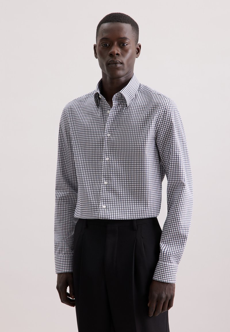 Witte overhemd met een klein zwart geruit patroon; heeft een klassieke kraag en knoopsluiting, gecombineerd met zwarte broek.