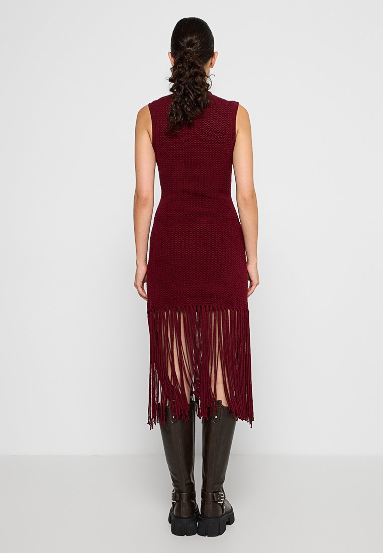 Vestido de punto burdeos con un cuerpo ajustado y un dobladillo largo con flecos. Modelo combinado con botas altas de cuero marrón.