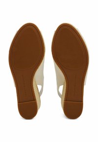 White wedge sandals with an open design, featuring a textured upper and a rubber sole. Brand name is embossed on the sole.
