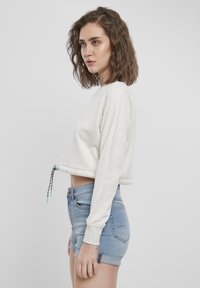 Kortsvetter i lys grått materiale med lange ermer og snøring i bunnen. Kombinert med blå denimshorts med oppbrett.