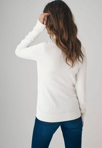 Fehér, hosszú ujjú pulóver, karcsú fazonnal, bordázott mandzsettákkal és hempergedéssel, sötétkék farmerral párosítva. Puha tapintású, minimalista dizájn.