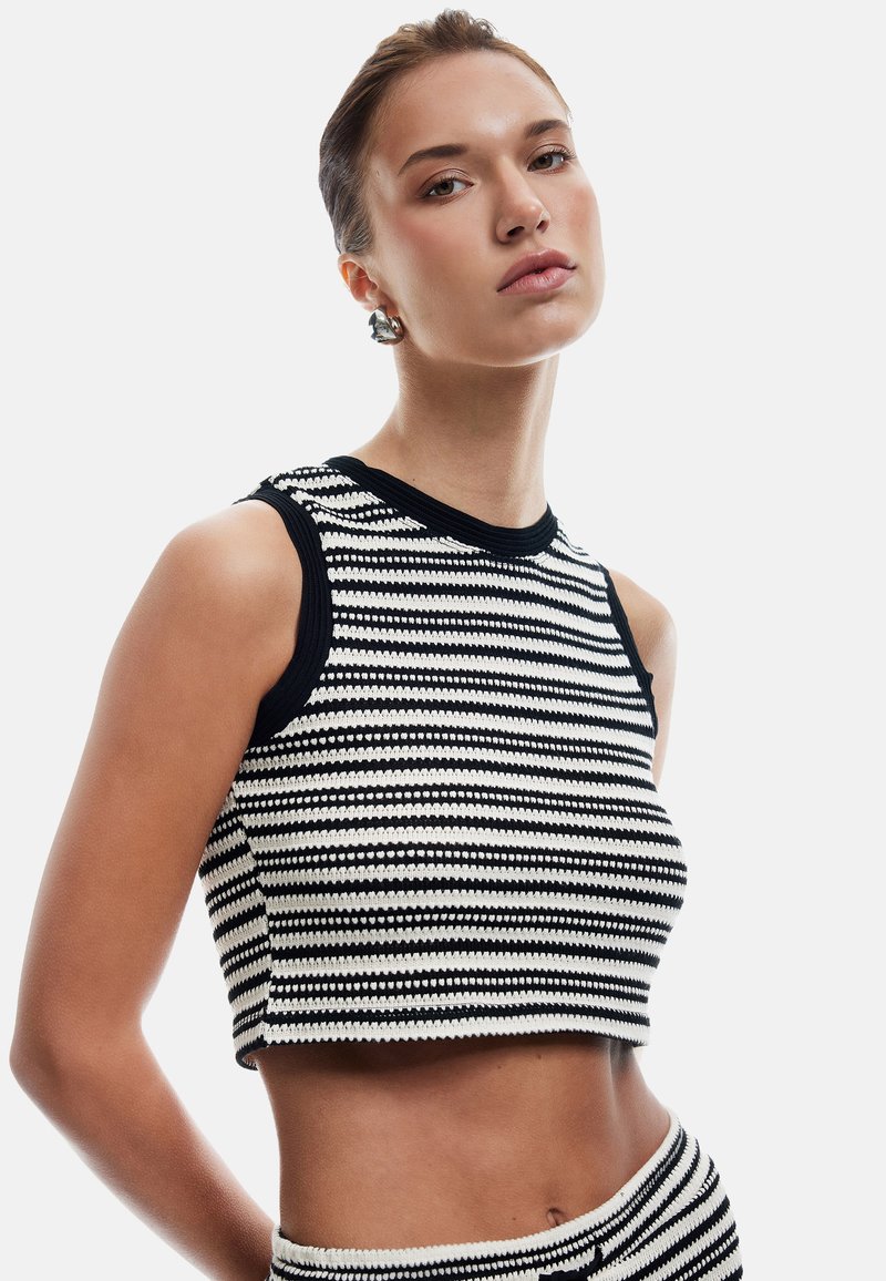Zwart-wit gestreepte crop top met geribde halslijn en mouwopeningen; textuur gebreide stof; aansluitend ontwerp.