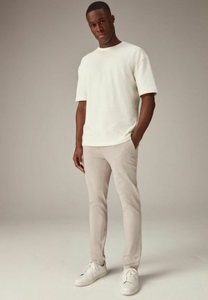 Lys grå t-shirt, afslappet pasform, med korte ærmer; parret med beige slim-fit bukser og hvide sneakers. Enkel design, minimale detaljer.