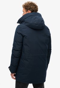 Granatowa ocieplana parka z dużym kapturem, gładką fakturą, subtelnym logo na plecach oraz regulowanymi mankietami.