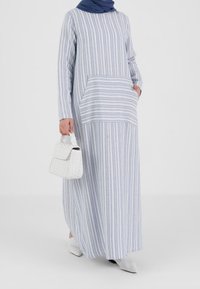 Robe longue rayée en bleu clair et blanc, avec une poche avant. Assortie à un sac tressé blanc et des chaussures blanches texturées.